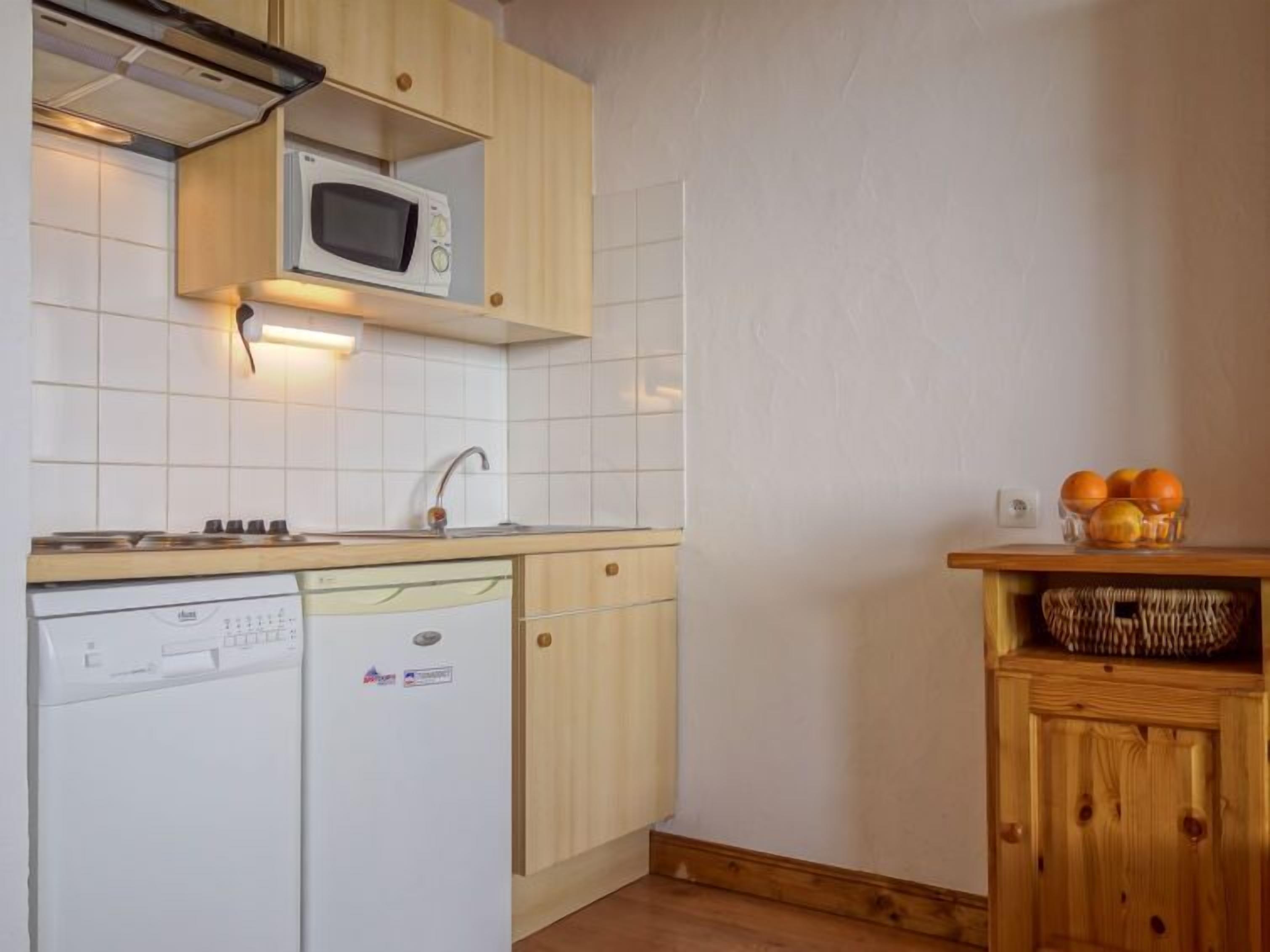 Une cuisine compacte équipée d’un four à micro-ondes, d’un lave-vaisselle et de meubles de rangement en bois.
