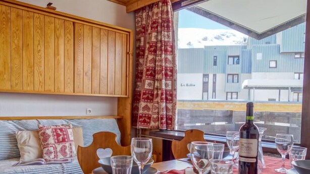 A cozy dining area with a wooden table set for two, a red table runner, and a bottle of wine. - Les Genepis (Val Claret) by Interhome (Tignes)