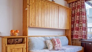 A wooden bed with a striped mattress, a wooden cabinet with a basket, and a window with patterned curtains. - Les Genepis (Val Claret) by Interhome (Tignes)