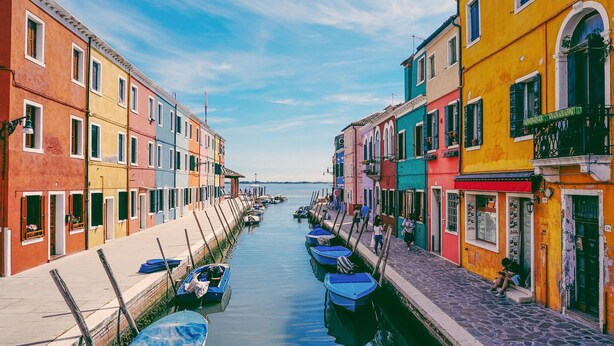 A narrow canal flanked by colorful buildings with boats docked along the sides.