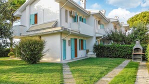 A two-story building with a white facade, blue shutters, and a small garden area with a stone pathway.