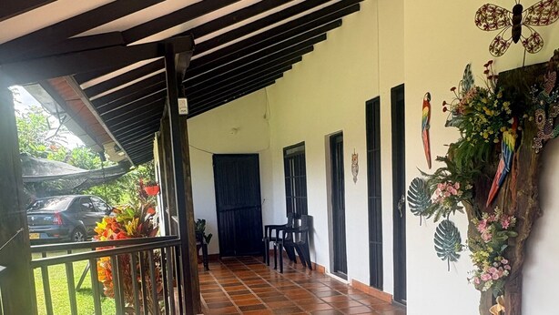 A covered outdoor area with a tiled floor, a gate, a car parked outside, and a wall with decorative elements. - Finca Campestre J&J (Quimbaya)