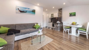 Una sala de estar moderna con un sofá gris, una mesa de centro de vidrio y un comedor con una mesa y sillas blancas.