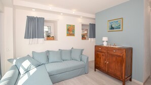 Una habitación con un sofá azul claro, un armario de madera y dos cuadros en la pared.