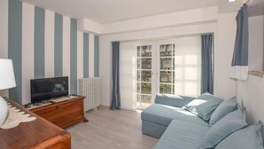Una habitación con televisión sobre un aparador de madera, un sofá y un ventanal con cortinas.