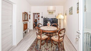 Un comedor con una mesa redonda, sillas, un tapete estampado, un piano y obras de arte colgadas en la pared.