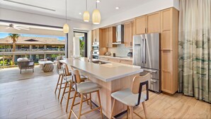 Una cocina moderna con una isla grande, electrodomésticos de acero inoxidable, armarios de madera y vistas a una piscina y un área de estar al aire libre.