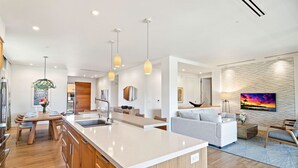 Una cocina moderna con una isla grande, luces colgantes y un comedor con mesa y sillas de madera.