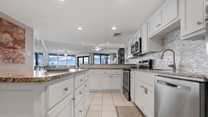 Una cocina moderna con armarios blancos, encimeras de granito, electrodomésticos de acero inoxidable y un amplio ventanal con vistas al exterior.