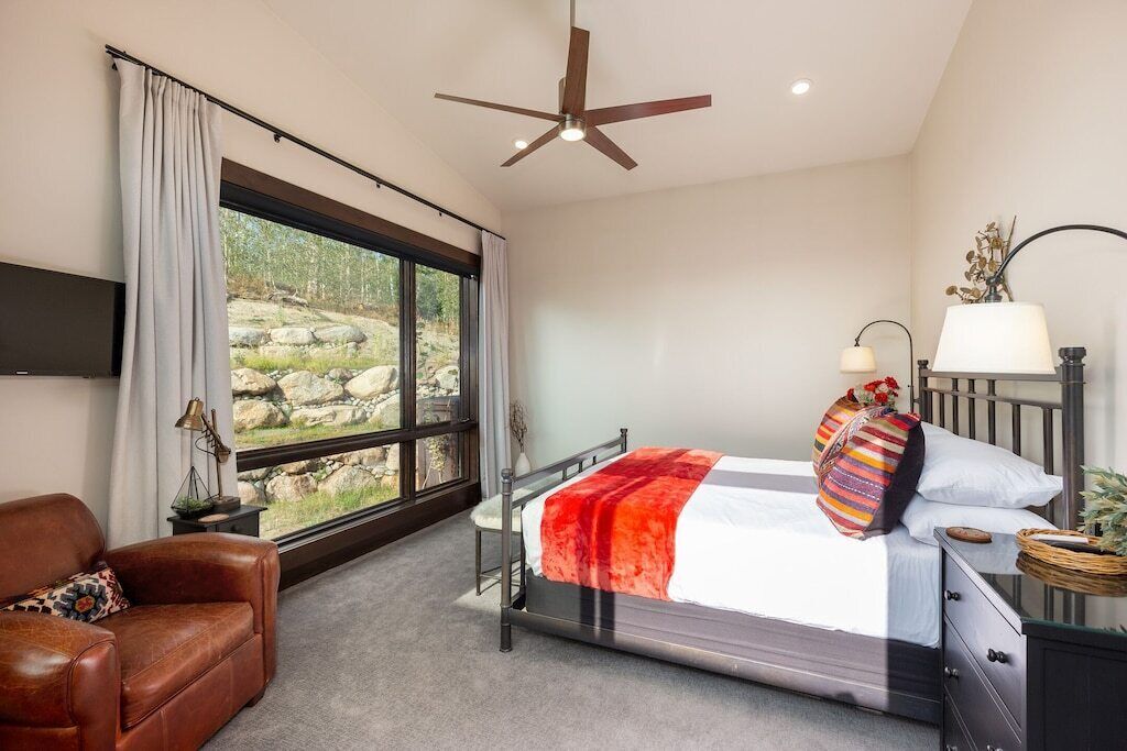 Ein Schlafzimmer mit Bett, Schreibtisch, Stuhl, Deckenventilator und einem großen Fenster mit Blick auf Felsen.
