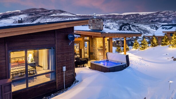 Eine Holzhütte mit Whirlpool und Essbereich, umgeben von schneebedeckten Bergen.