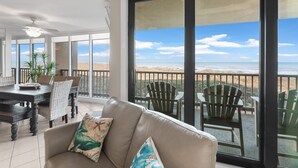 Een ruim balkon met uitzicht op het strand, voorzien van een tafel, stoelen en een bank.