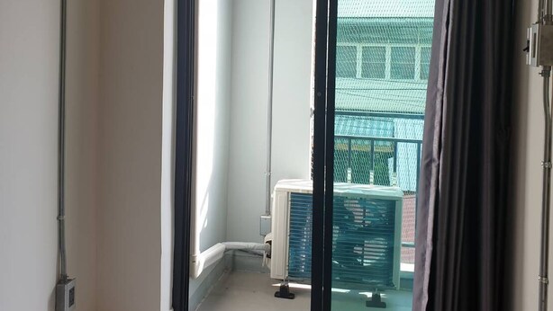 A hotel room with a sliding glass door leading to a balcony, an air conditioning unit mounted on the wall, and a window with a curtain.