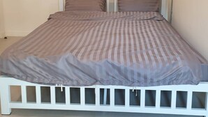 A single-bed room with a white frame, a striped bedspread, and two pillows.