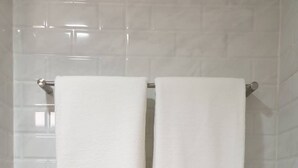 A bathroom with white tiled walls and two white towels hanging on a metal towel rack.