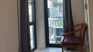 A room with a sliding glass door leading to a balcony, an air conditioning unit mounted above the door, and a wooden chair in the corner.
