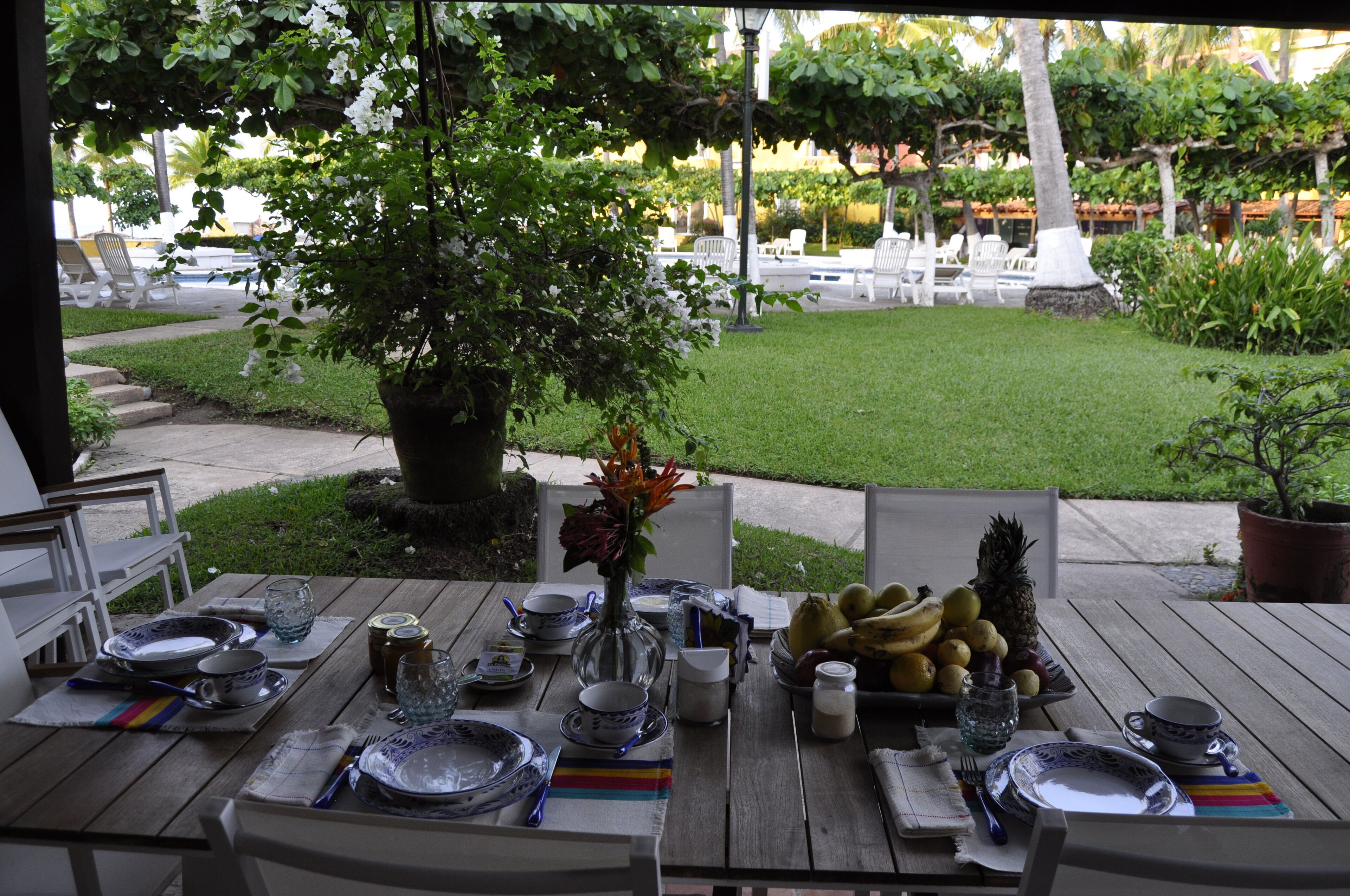 Un espace extérieur aménagé pour les repas, avec une table dressée et entourée de chaises et de plantes en pot.