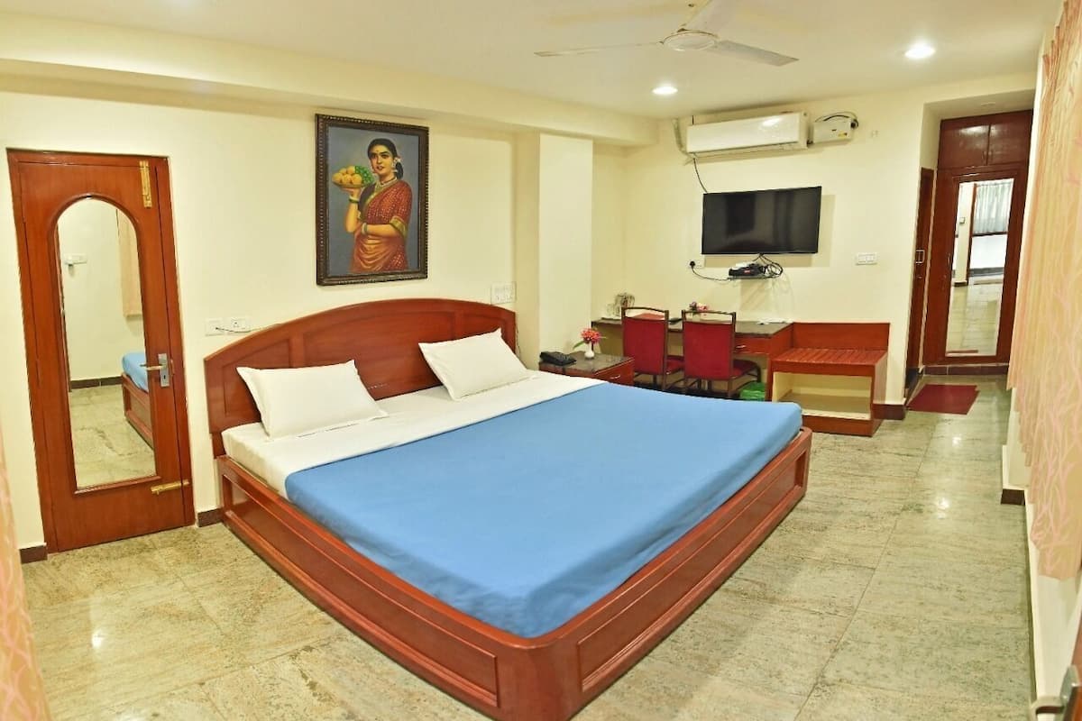 A hotel room with a bed, a desk, a chair, a television, and a mirror.