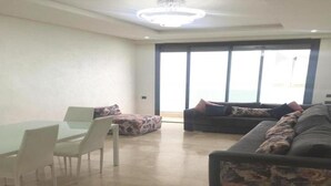 A spacious living area with a dining table, sofas, and a large window providing a view of the outdoors. - Bay Inn (Tirukalukundram)