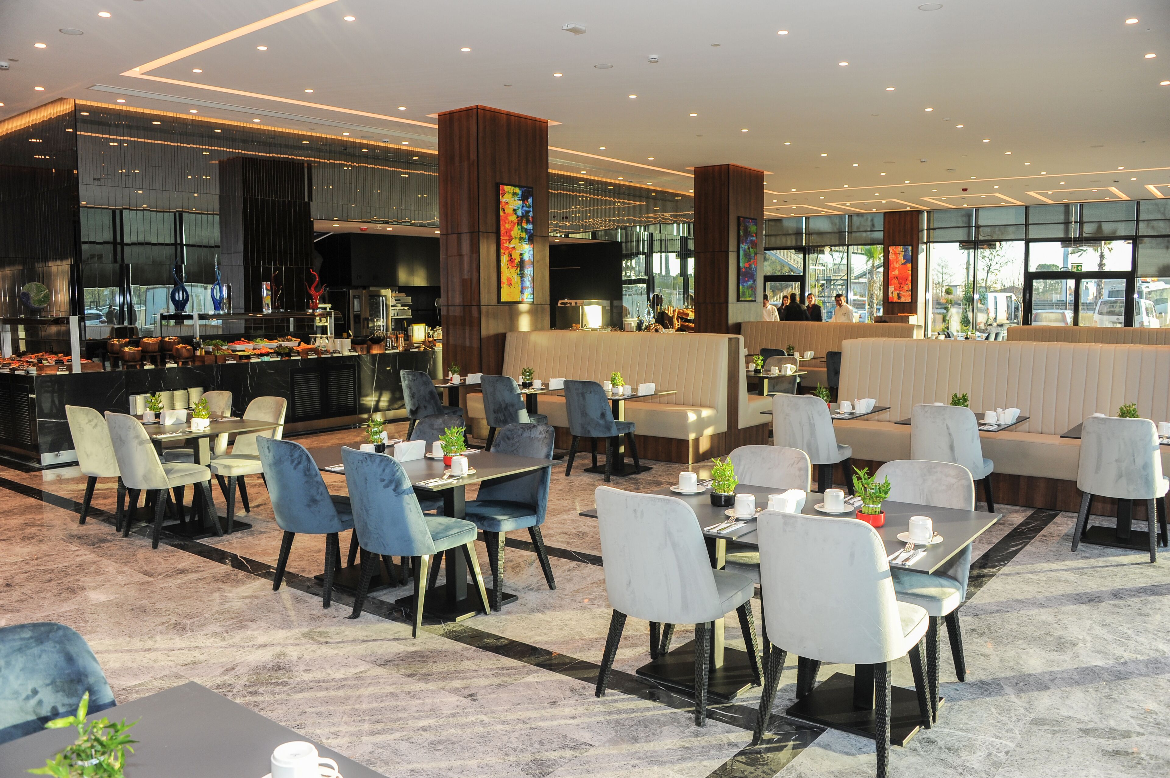 Een modern restaurant met een bar, verschillende zitplaatsen zoals tafels en hoekbanken, en uitzicht op de stad door grote ramen.
