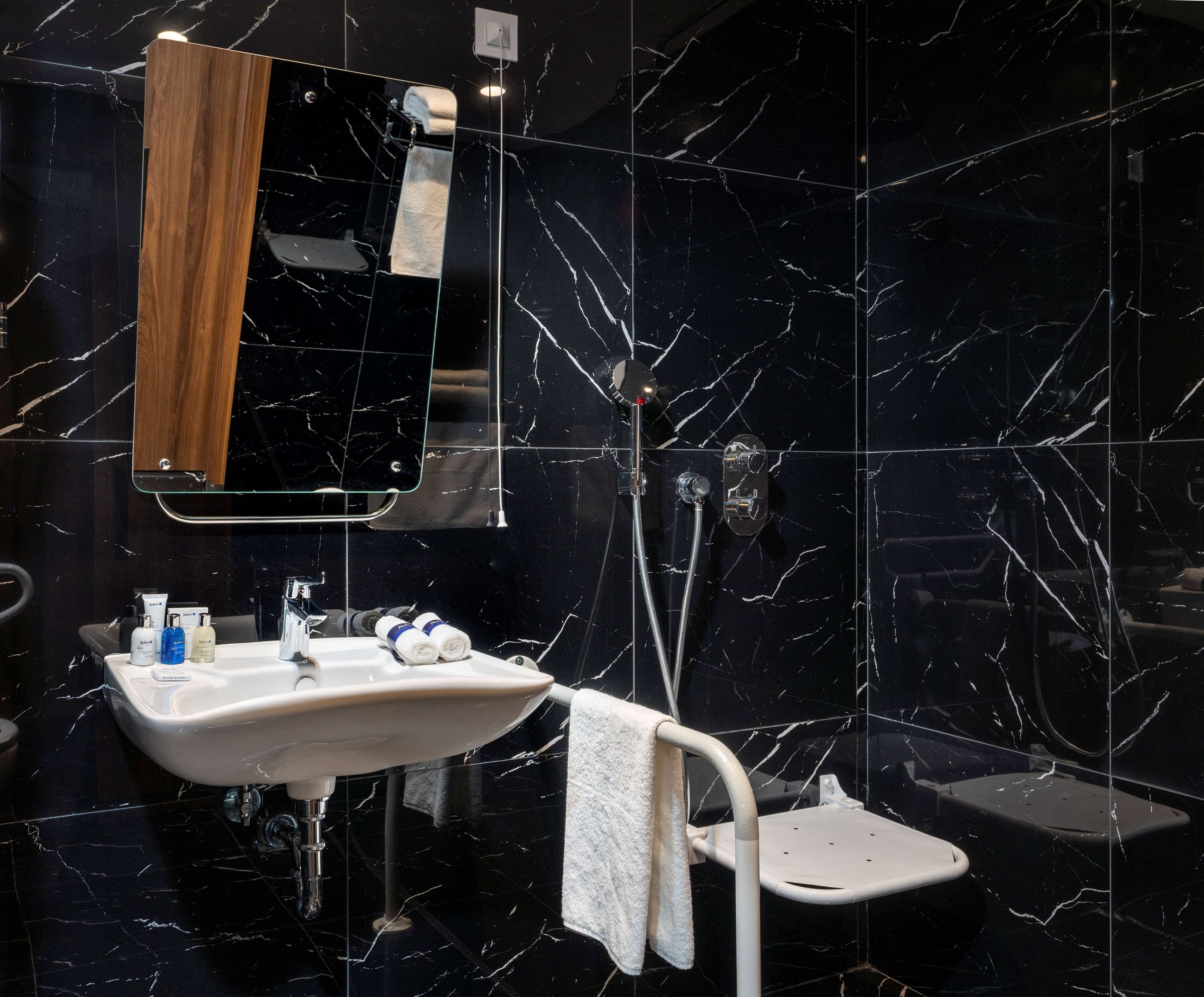 A modern bathroom with a marble backsplash, a wooden medicine cabinet, a white sink, and a handheld showerhead.