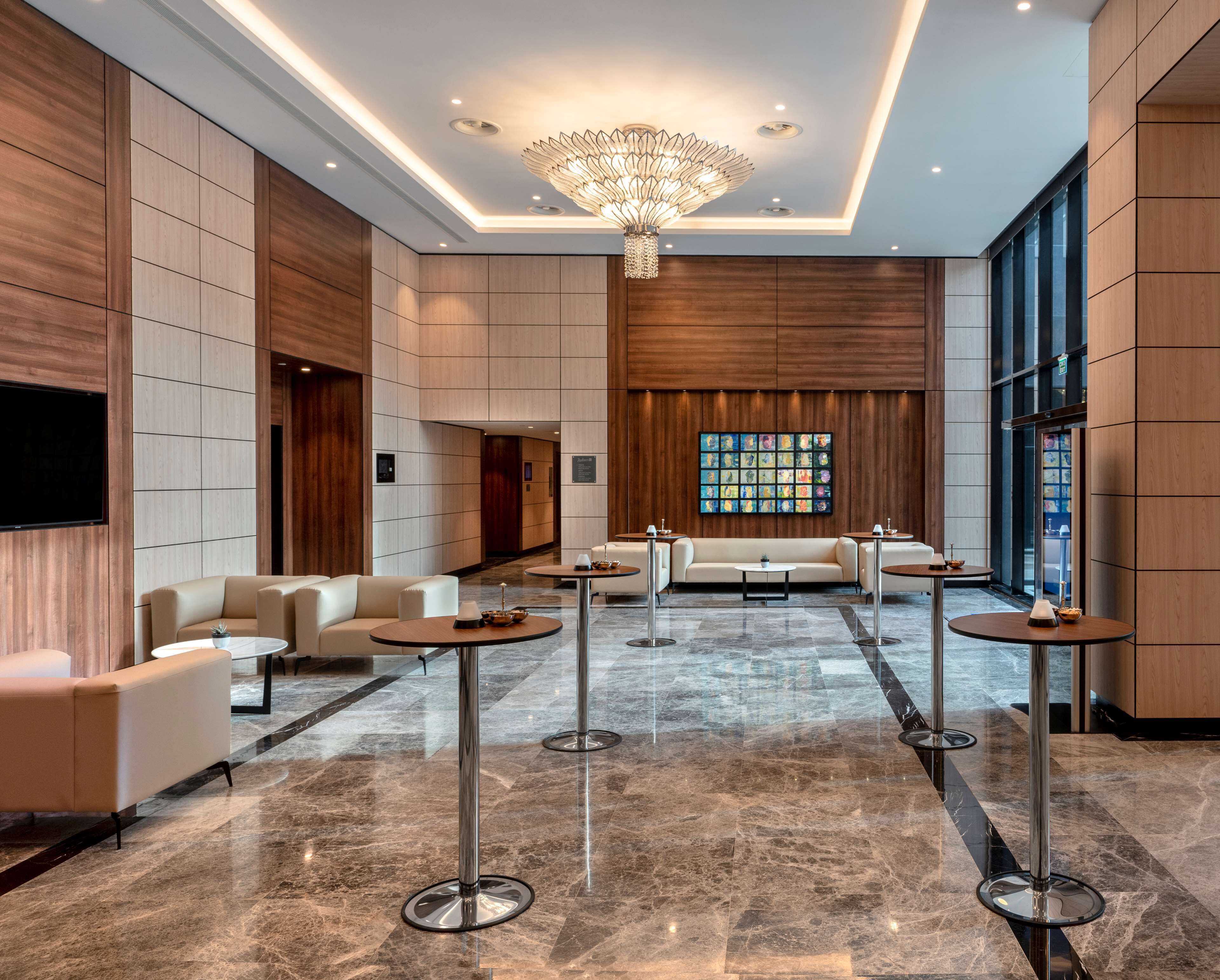 Un hall d’entrée spacieux avec un plafond haut, un lustre central et un espace détente avec des canapés et des tables rondes.