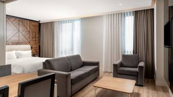 Une chambre d’hôtel moderne équipée d’un lit, d’un canapé, d’un fauteuil, d’une table basse et d’un téléviseur.