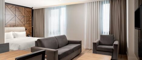 Een moderne hotelkamer met een bed, een bank, een stoel, een salontafel en een televisie.