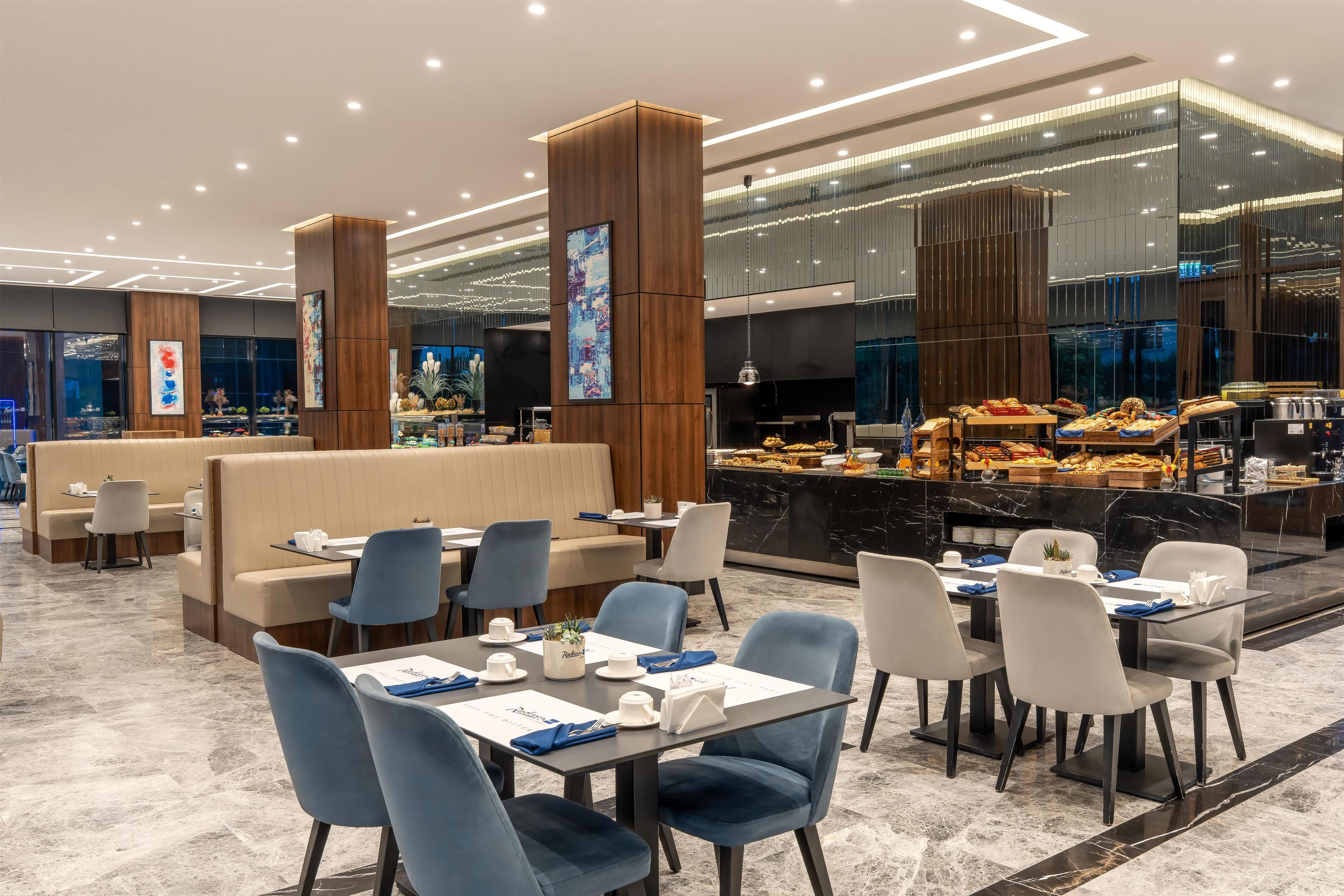 A modern hotel lobby with seating areas, a buffet, and a large digital screen.