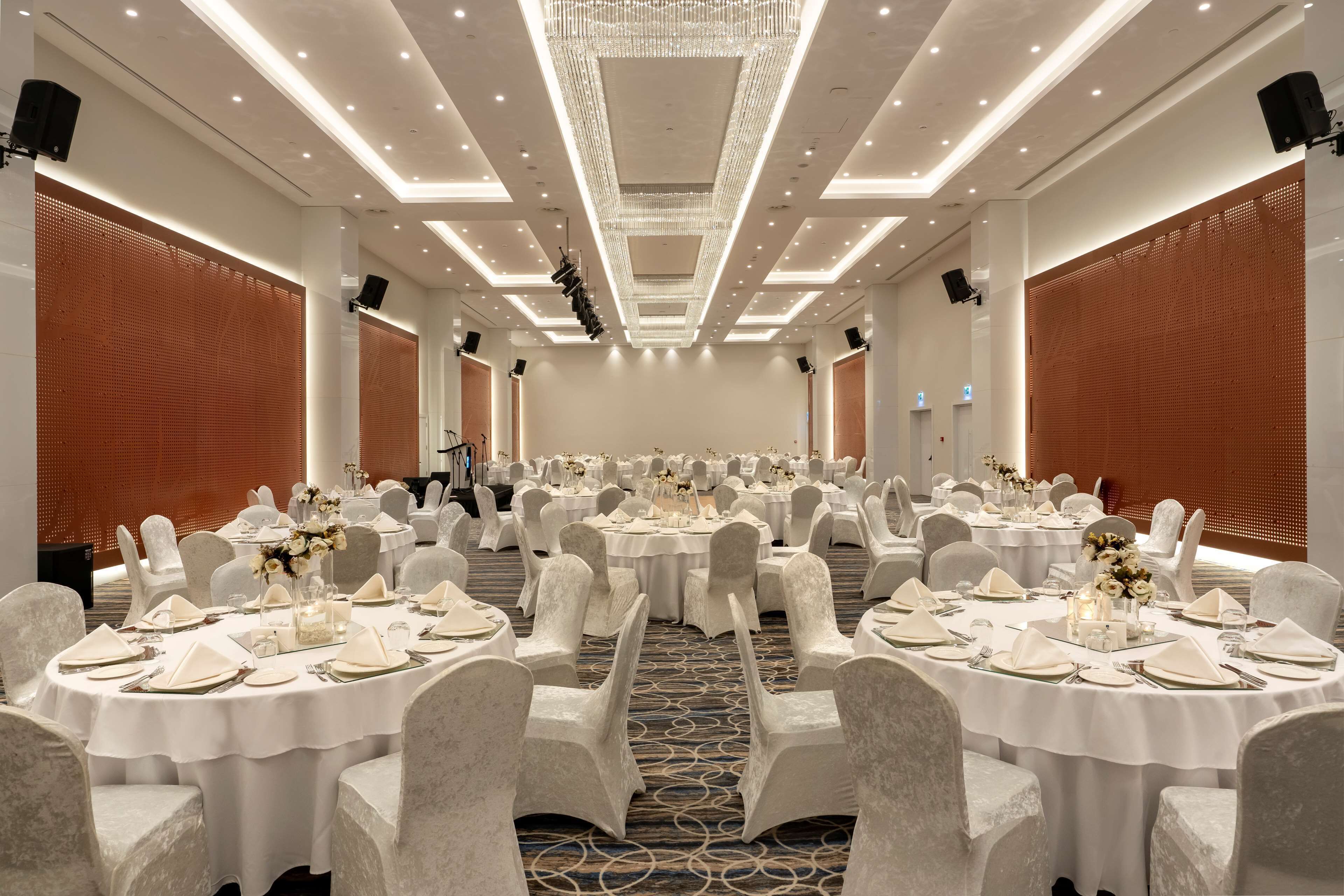 Un salón de banquetes con mesas redondas dispuestas para eventos, con manteles blancos, sillas y centros de mesa florales.