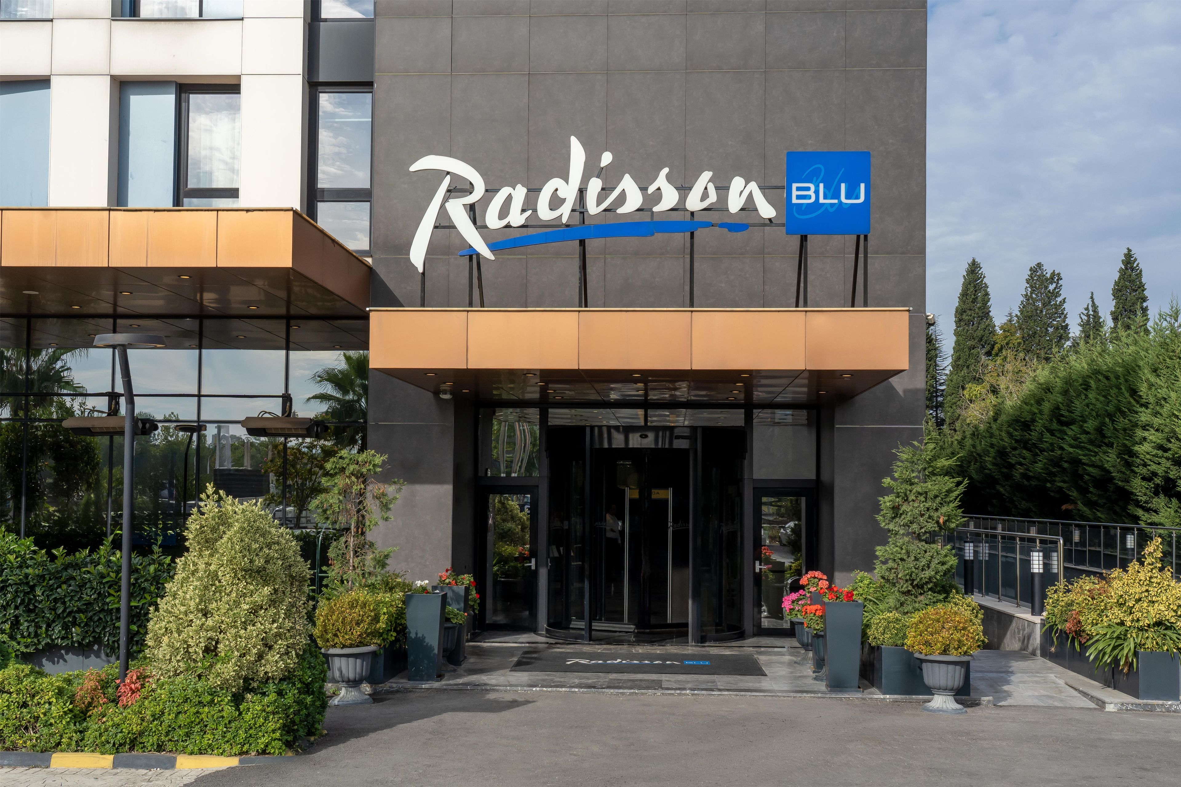 A Radisson BLU hotel entrance with a modern facade, glass doors, and potted plants.