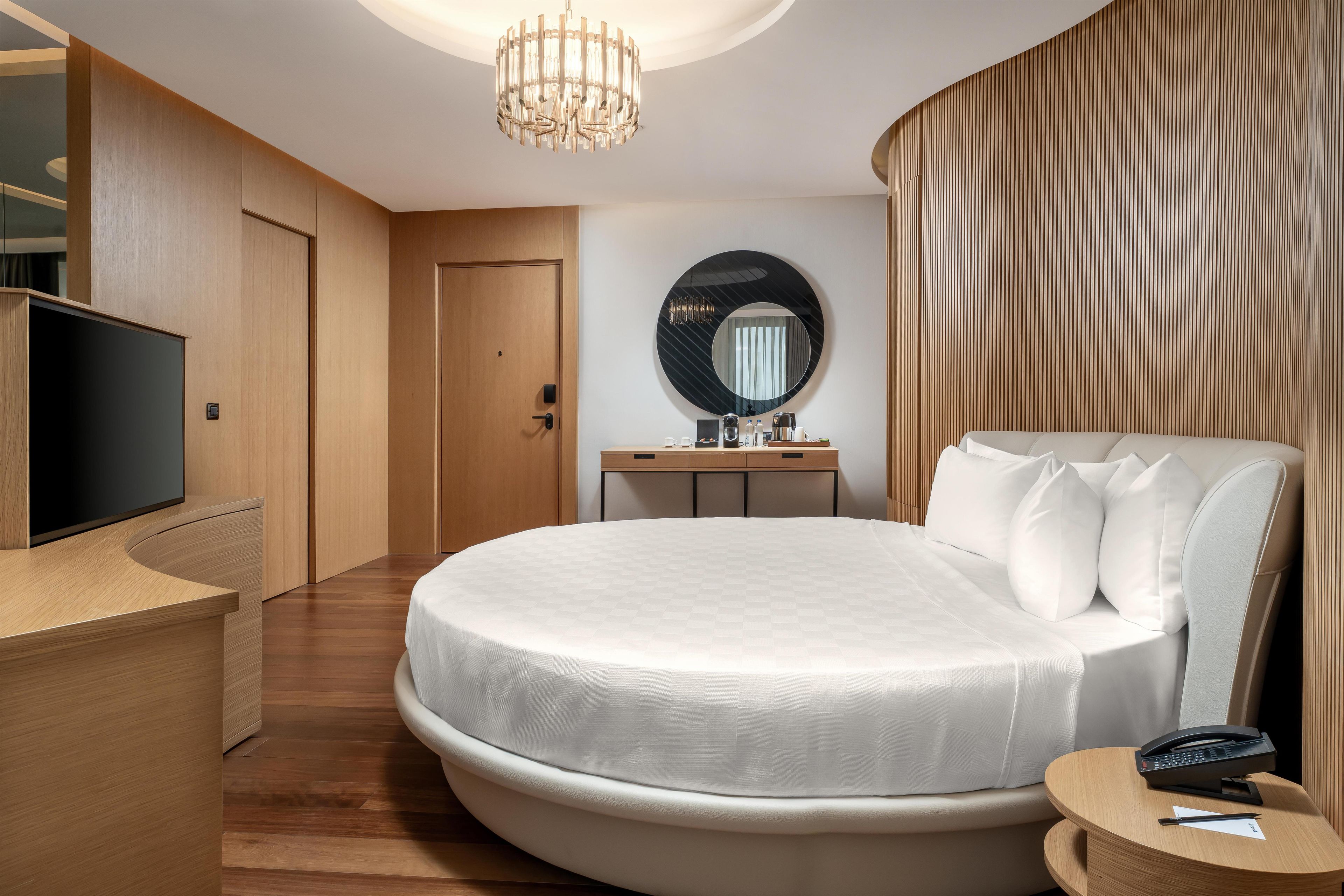 A modern hotel room with a large bed, a desk, a television, and a mirror.