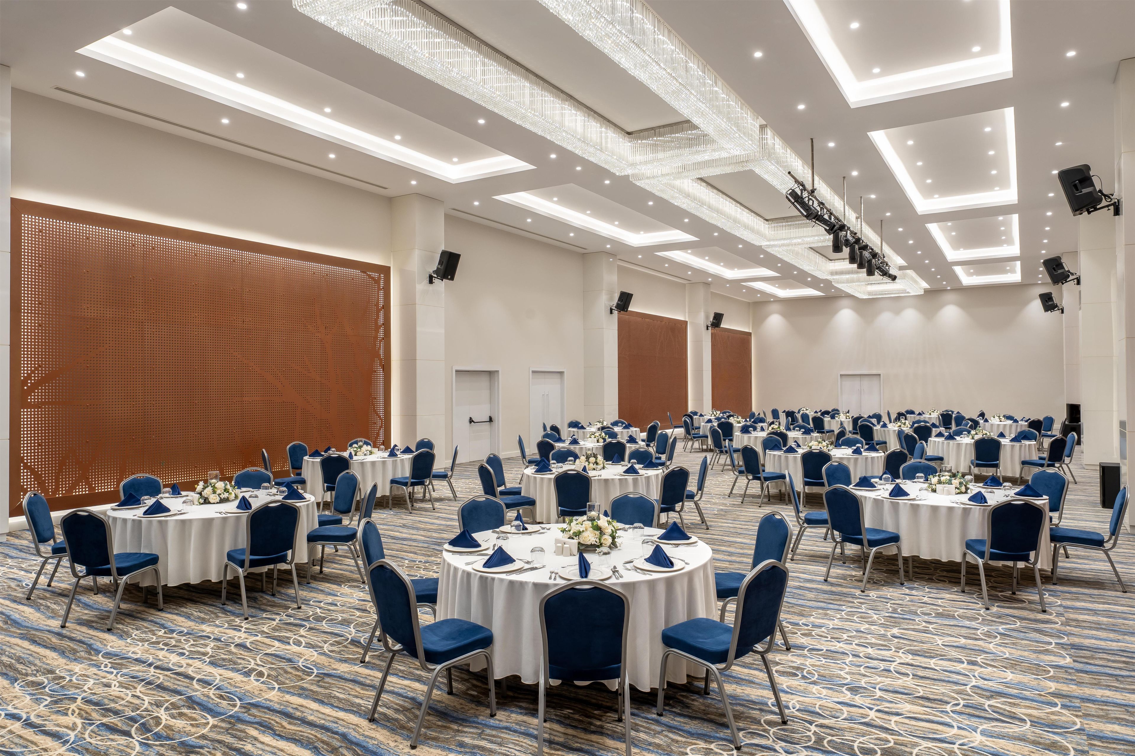 A large conference room with round tables, blue chairs, and white tablecloths.