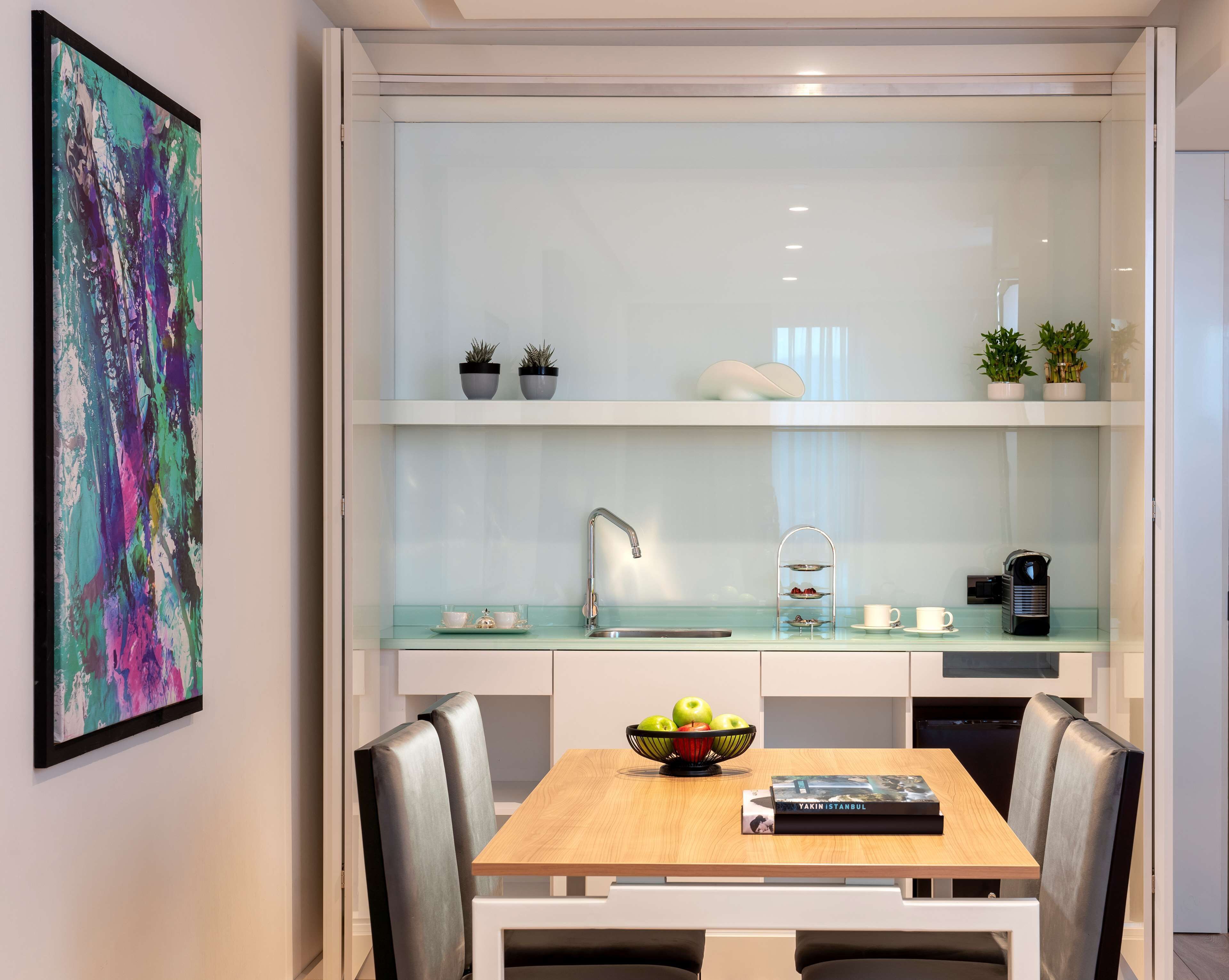 Cozinha moderna com painel de vidro, armários brancos e área de refeições com mesa e cadeiras de madeira.