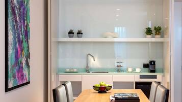 Cozinha moderna com painel de vidro, armários brancos e área de refeições com mesa e cadeiras de madeira.