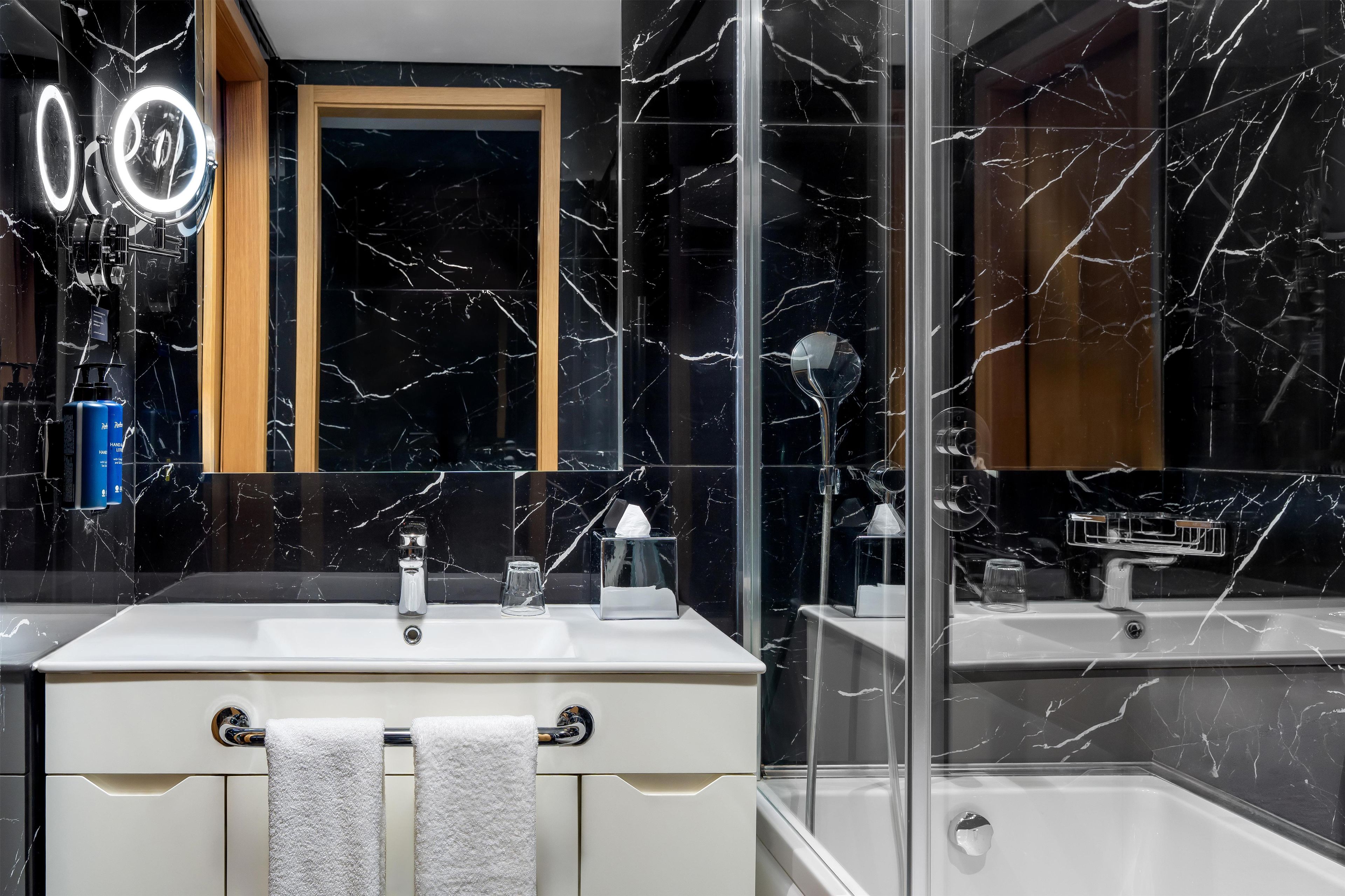 A bathroom with a black marble sink, a mirror, and a glass-enclosed shower.