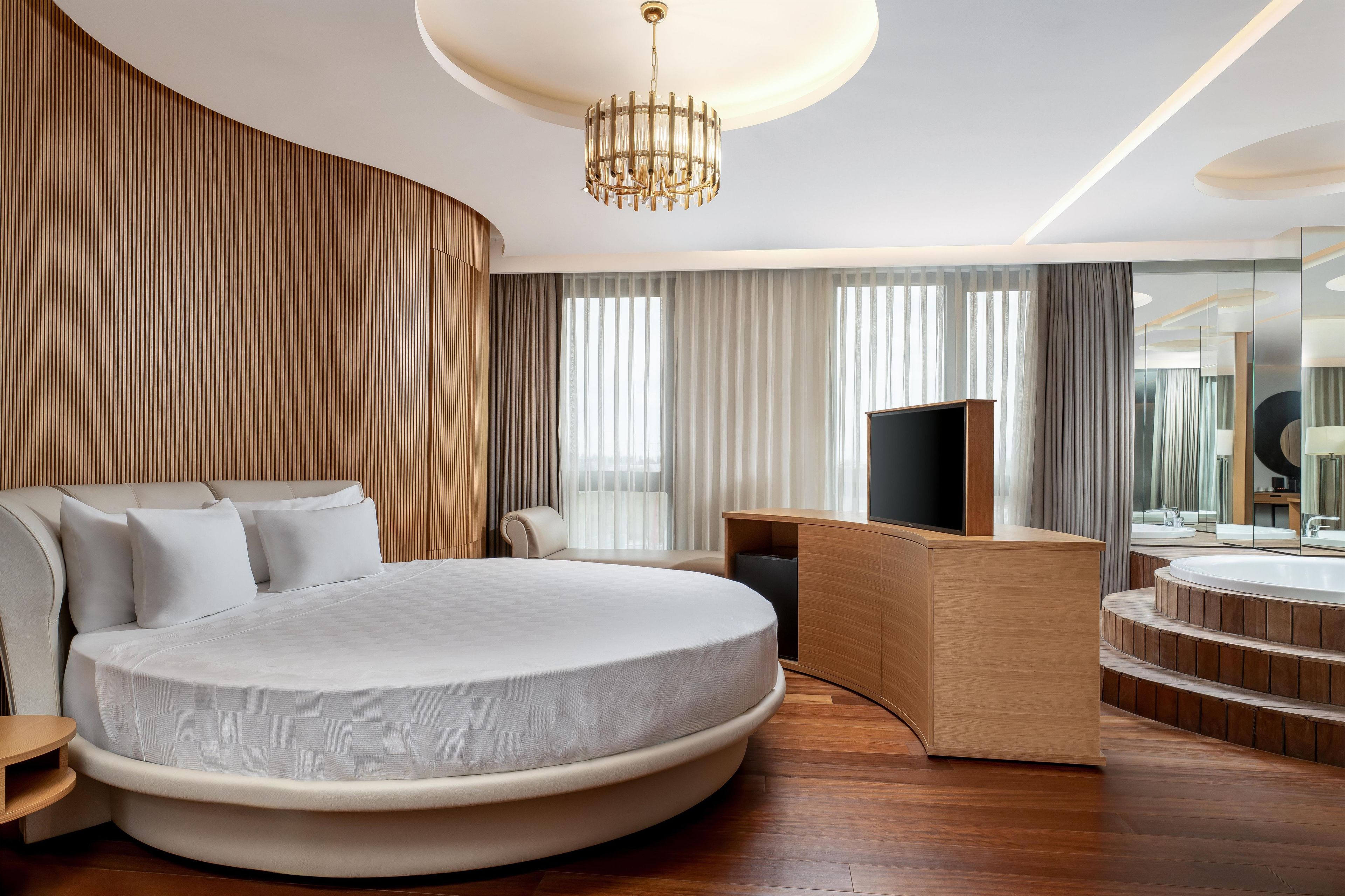 Un dormitorio moderno con una cama grande, un televisor y un tocador de madera con espejo.