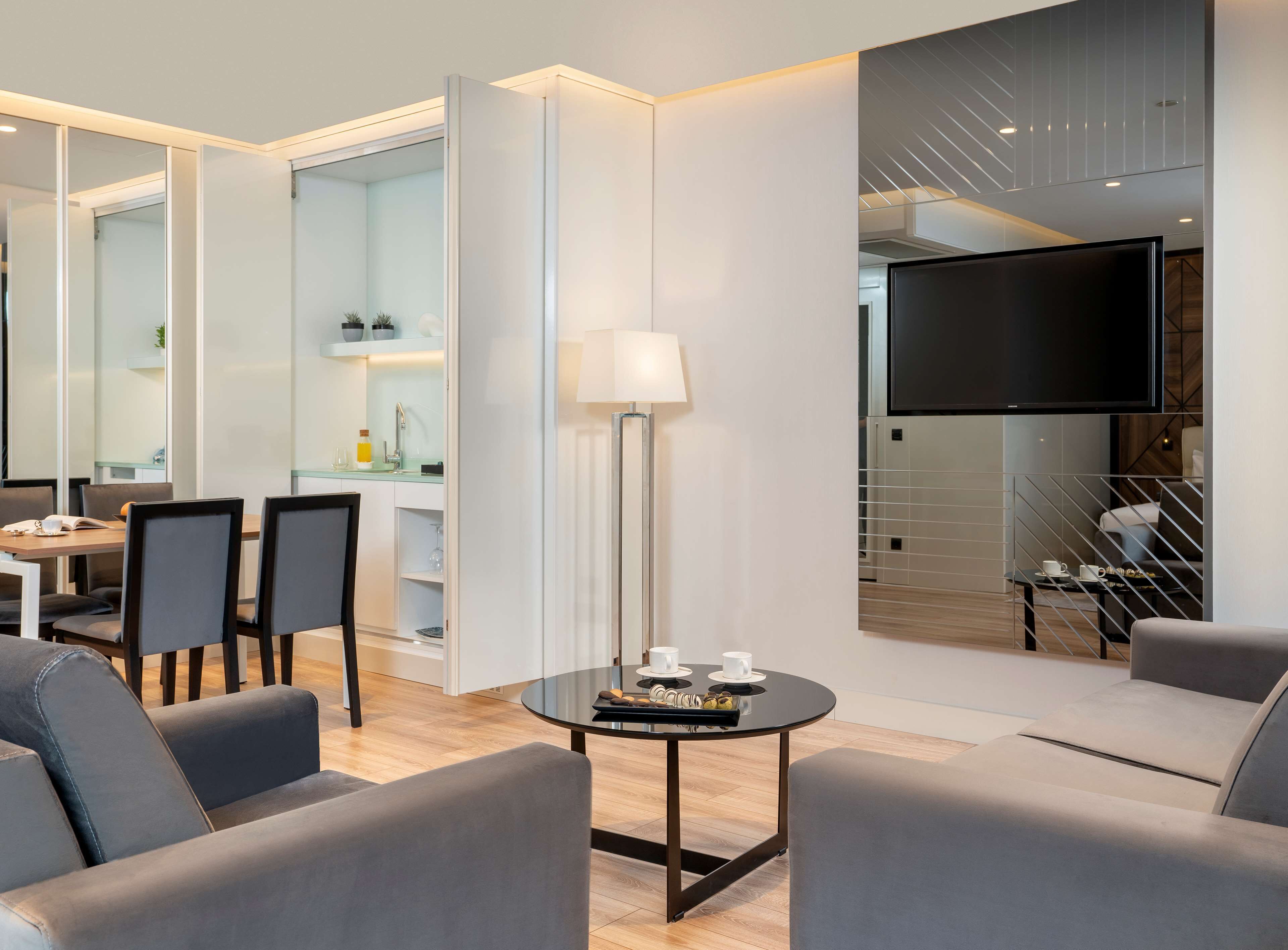Una habitación de hotel moderna con zona de comedor, televisor de pantalla plana y sofá.