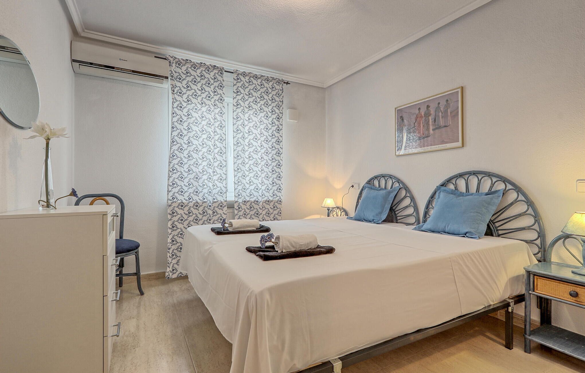 Ein ordentlich eingerichtetes Schlafzimmer mit Bett, Nachttischen, einem Sessel und einem Schreibtisch.