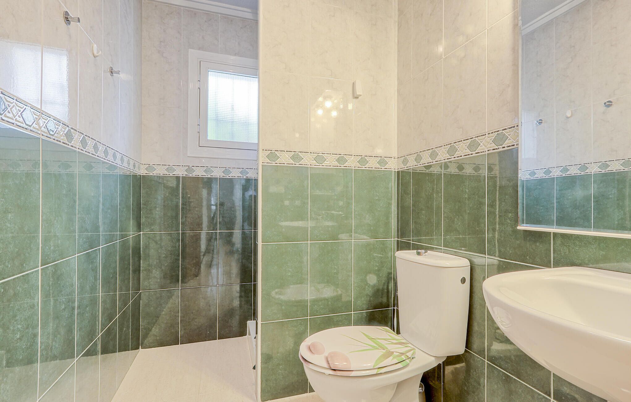 A bathroom with green tiles, a toilet, and a sink.