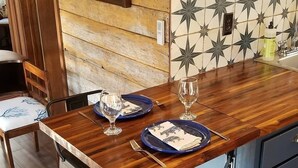 Una mesa de comedor de madera dispuesta con platos azules y copas de vino, un aparador azul y una silla con asiento negro.