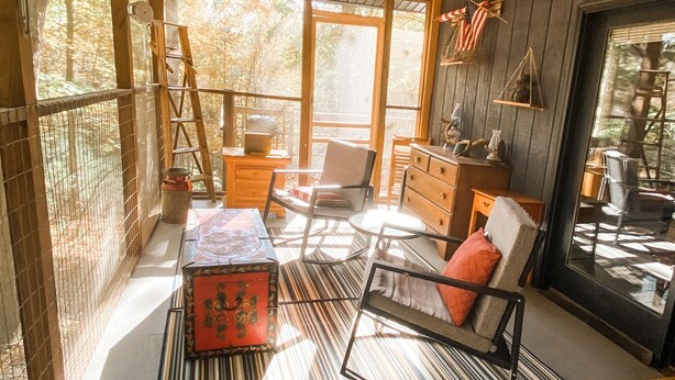 Interior acogedor de una cabaña con techo de madera, un ventanal grande y una alfombra a rayas.