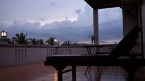 Une terrasse avec une table et des chaises, des palmiers et un ciel nuageux.
