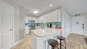 Et moderne køkken med hvide skabe, en central ø med barstole, rustfrie stålgre samt en backsplash i teal farve.