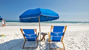 Two beach chairs with blue cushions and a matching blue umbrella on a sandy beach.