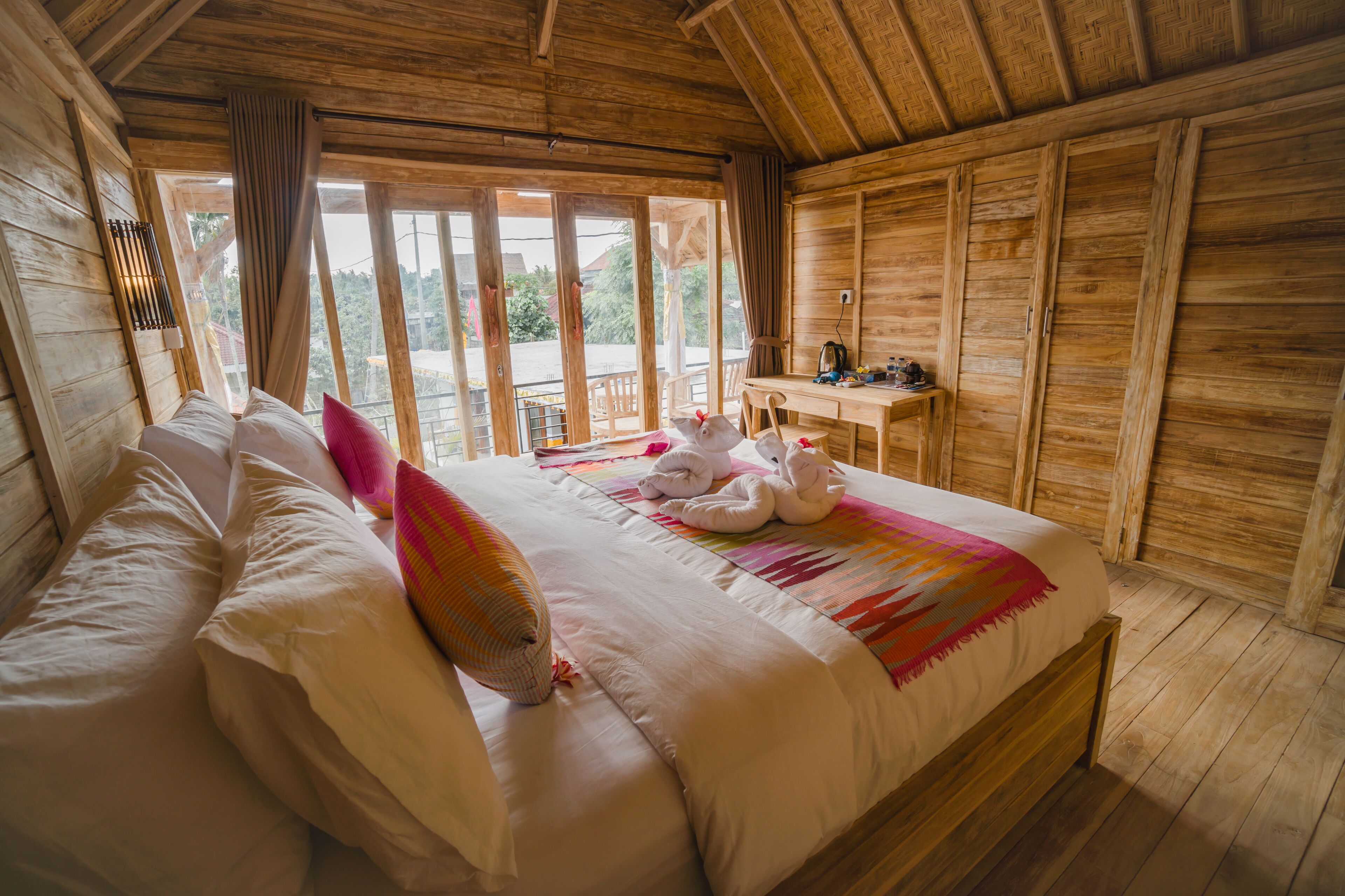 A wooden cabin bedroom with a large bed, a desk, and a view of the outdoors.