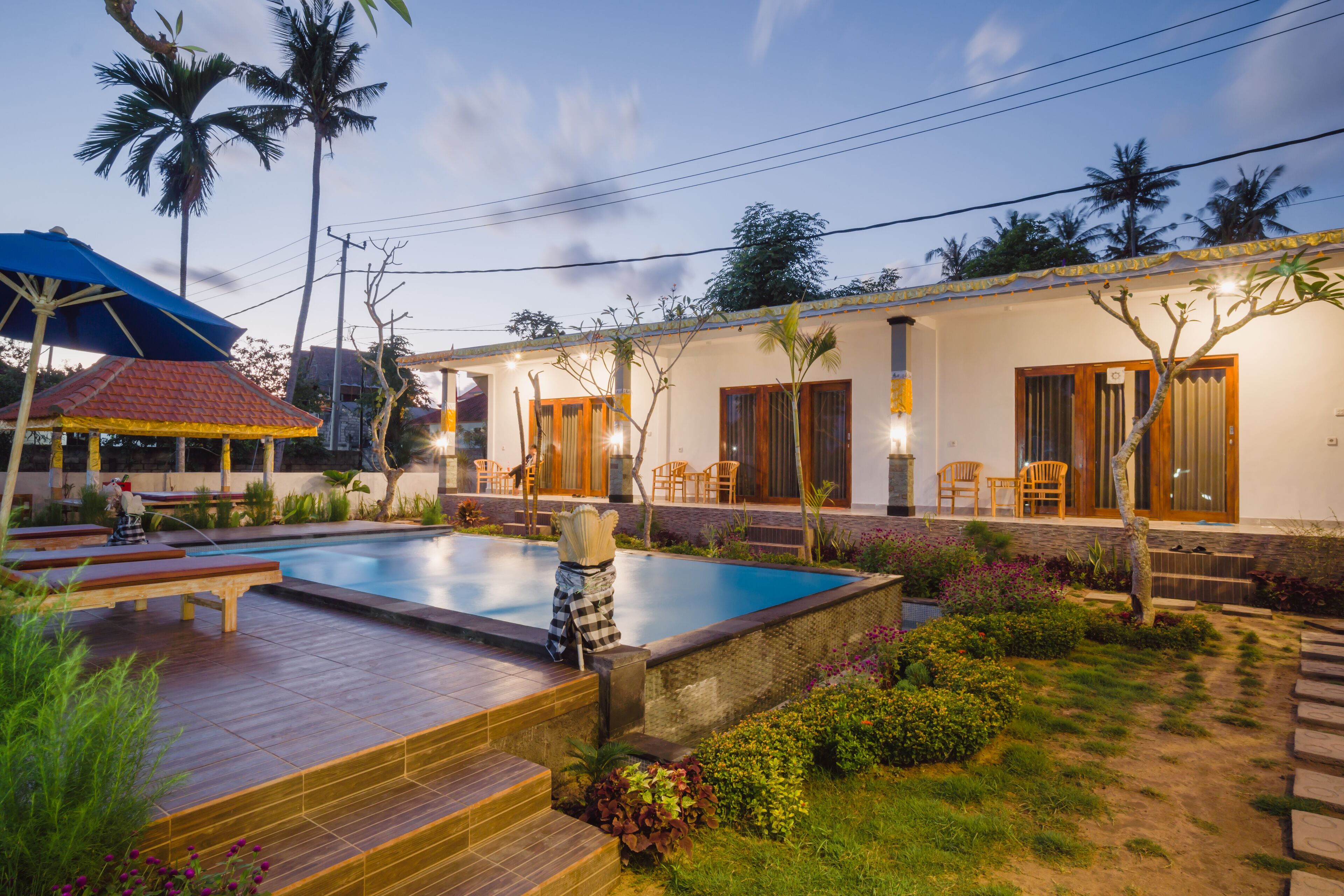 A swimming pool with lounge chairs, a covered seating area, and a building with wooden doors and windows.