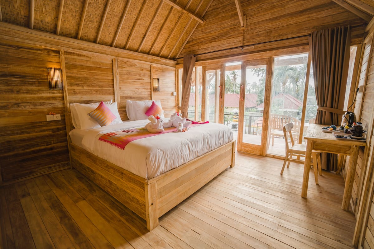 A wooden room with a bed, a table, and a view of the outside.