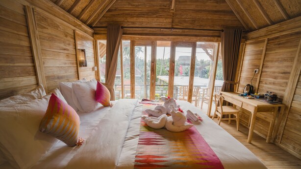A wooden cabin room with a large bed, a desk, and a view of the outdoors. - Pi Karya Beach (Penida Island)