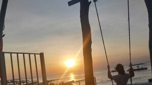 A beach scene with a swing set and a sunset in the background. - Pi Karya Beach (Penida Island)